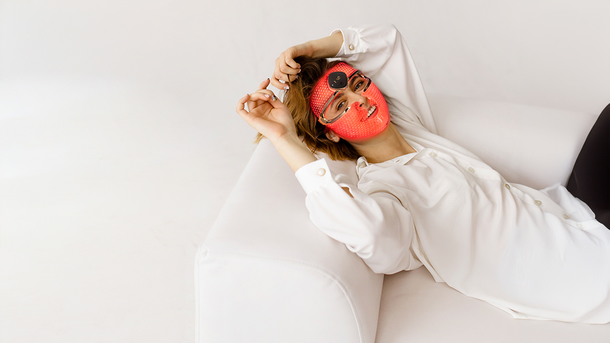 Woman on the couch using FAQ™ 202 LED face mask